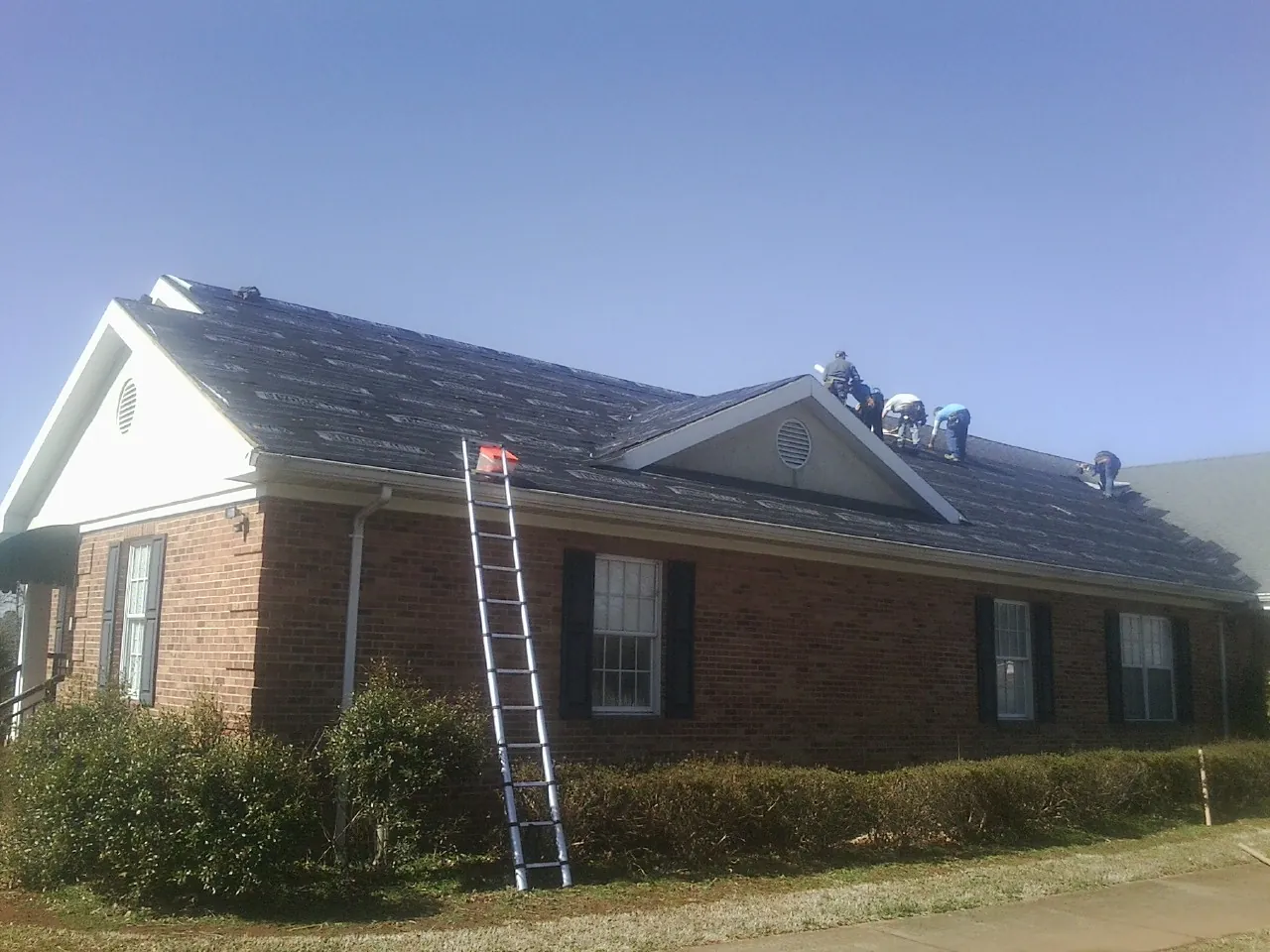 Crew tearing shingles off a brick ranch roof with a ladder set — Metal Roof Repair work by our crew in Ashville