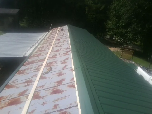 Old rusted panels beside newly installed green metal roofing — Wind Damage Roof Repair by Roofing Brothers in Ashville