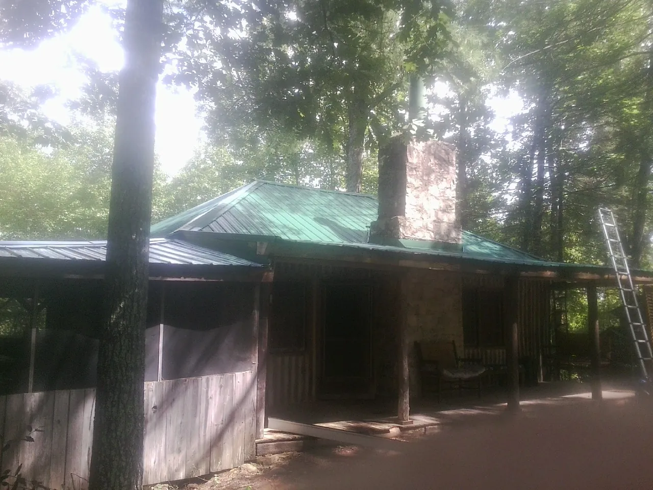Green metal roof and stone chimney above a log cabin porch in Ashville