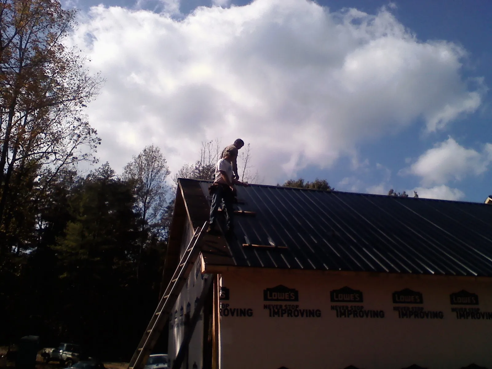 Roofer fastening dark metal panels high against a cloudy sky, from a Roof Inspection job in Ashville