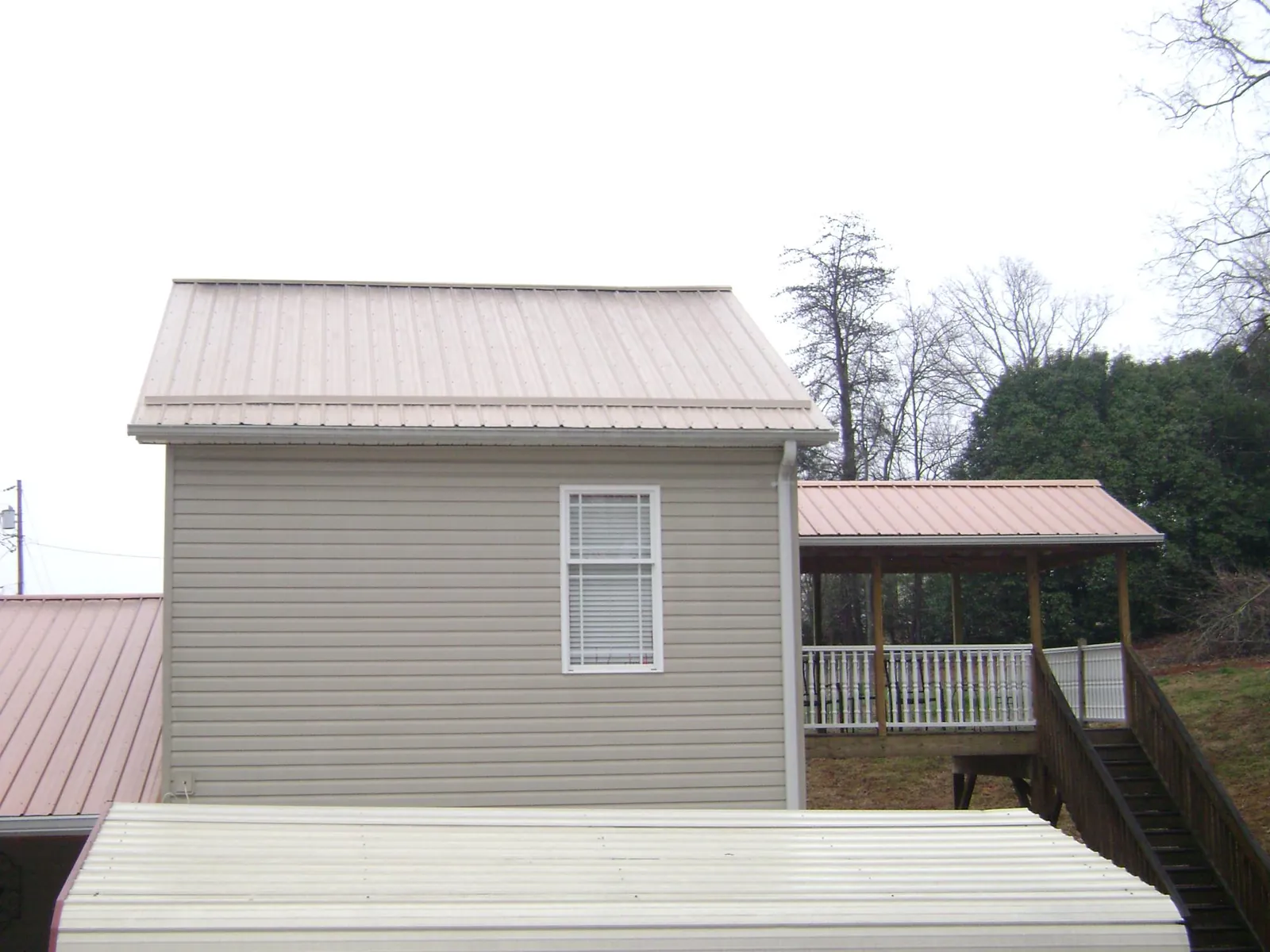 Tan metal roofs on a two story addition and attached porch, from a Roof Replacement job in Ashville